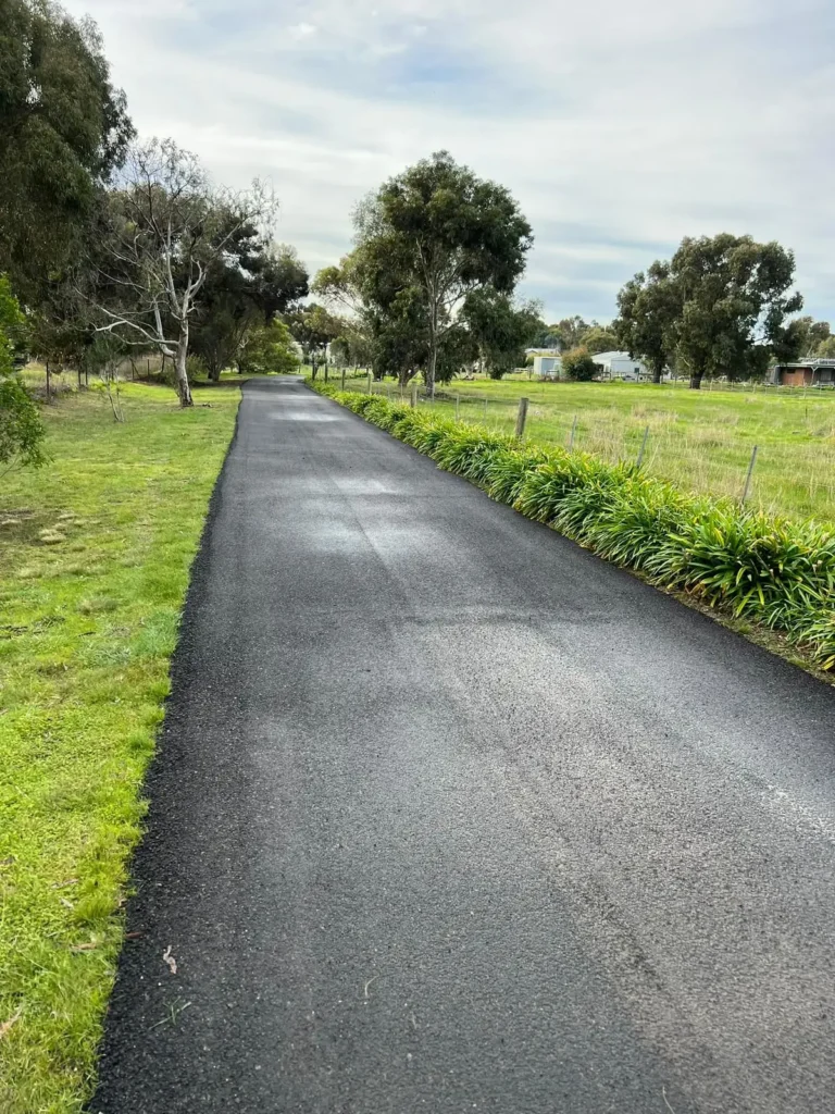 Newly paved asphalt driveway leading through a rural property